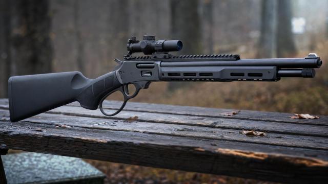 Čierna páková puška Smith & Wesson Model 1854 Stealth Hunter s kompaktnou optikou na loveckej lavičke.