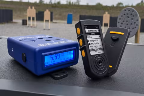 Competition Electronics ProTimerBT a Shooters Global SG Timer 2 položené vedľa seba na strelnici.