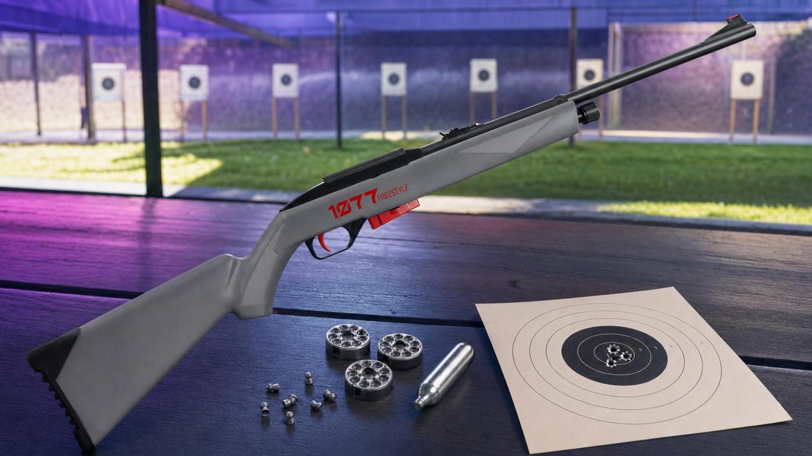 Crosman 1077 FreeStyle s rotačnými klipmi, CO₂ bombičkou a terčom na streleckom stole.