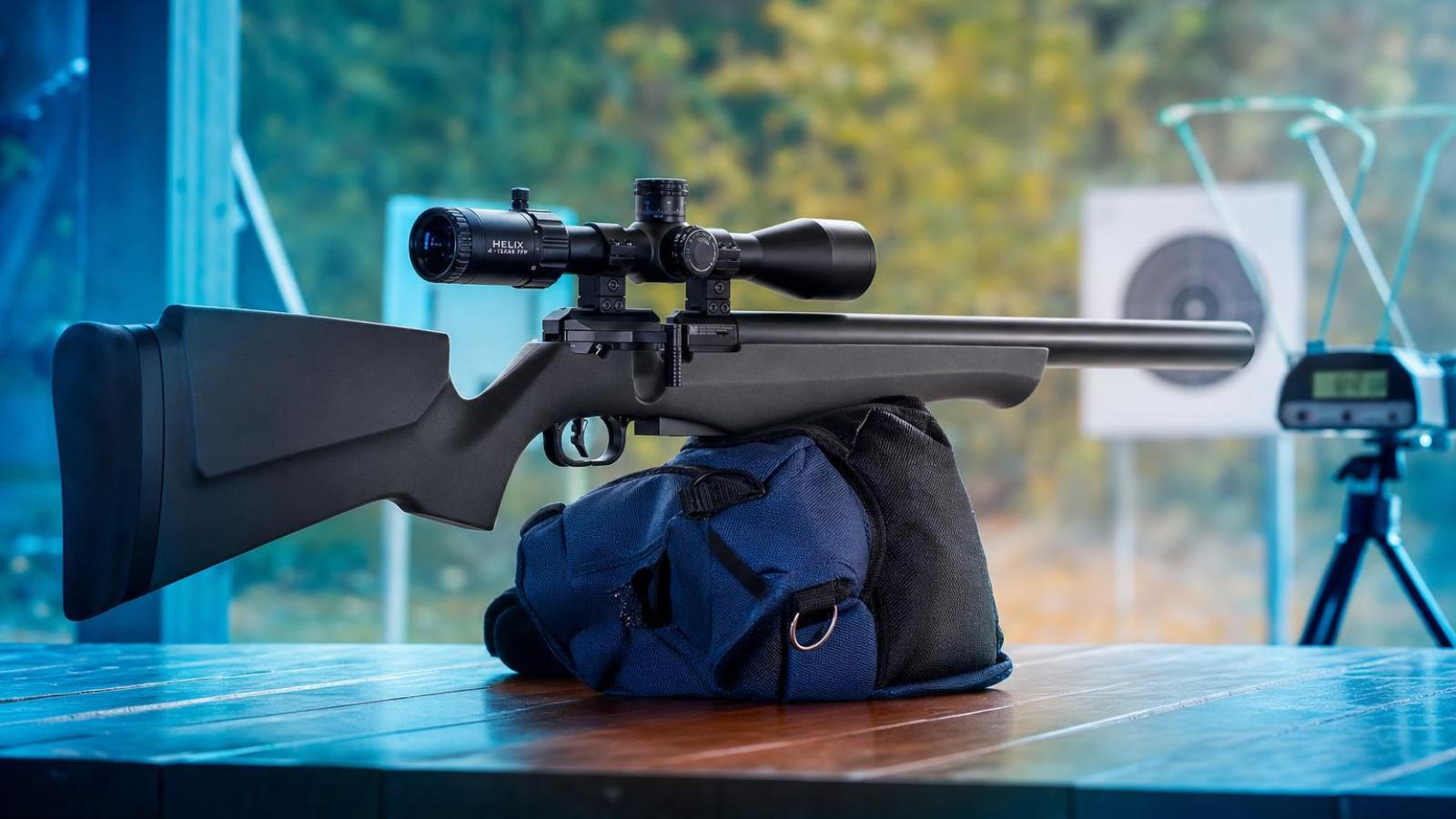 FX Airguns DRS Classic s orechovou pažbou a vzduchovým zásobníkom okolo hlavne na streleckom stole.
